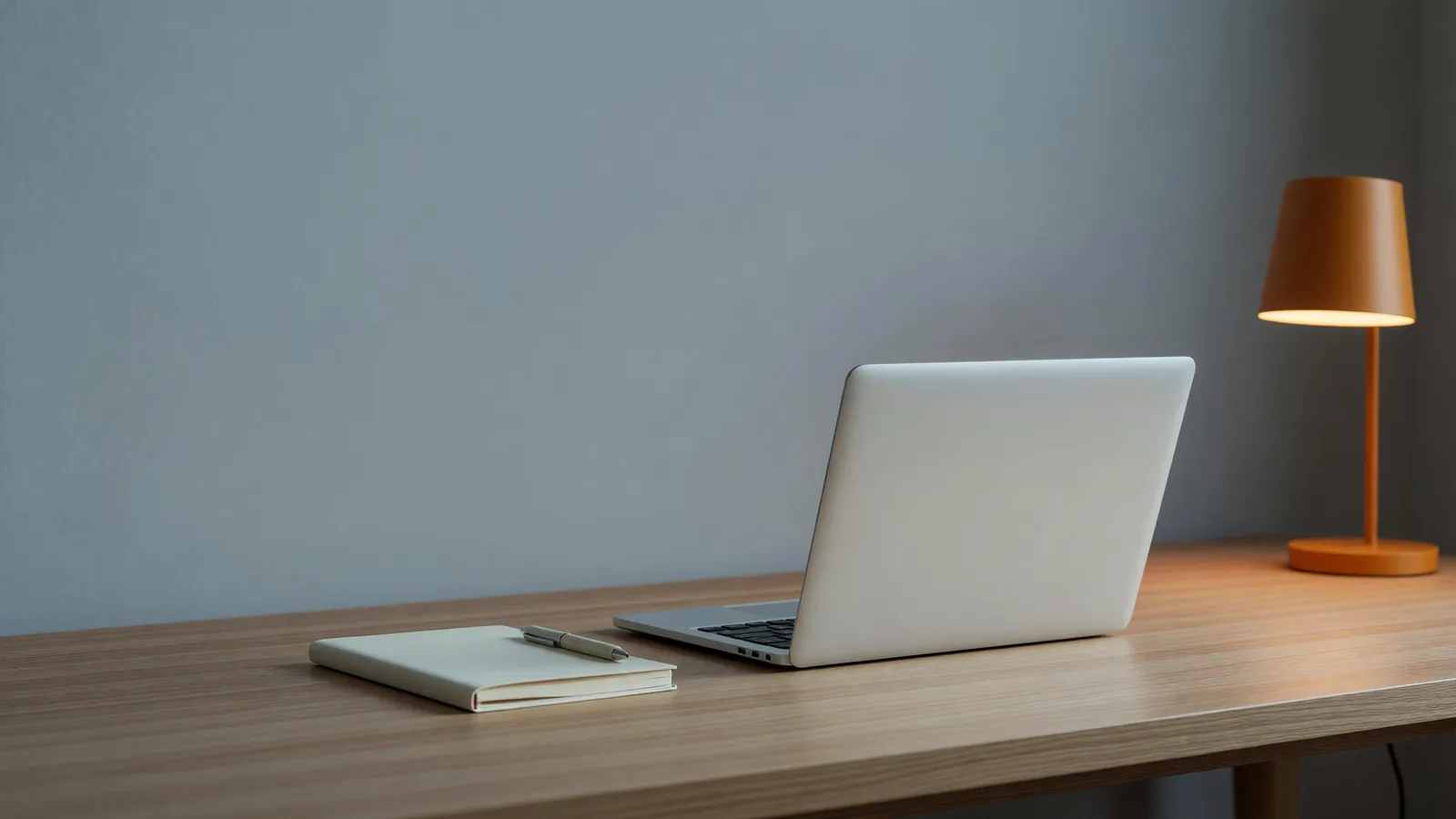 A closed aluminum laptop, notebook, and glowing amber lamp on a home-office desk, depicting Conway Research's Underdog, the fully on-device personal AI assistant that leads today's brief. Illustration: DeAI